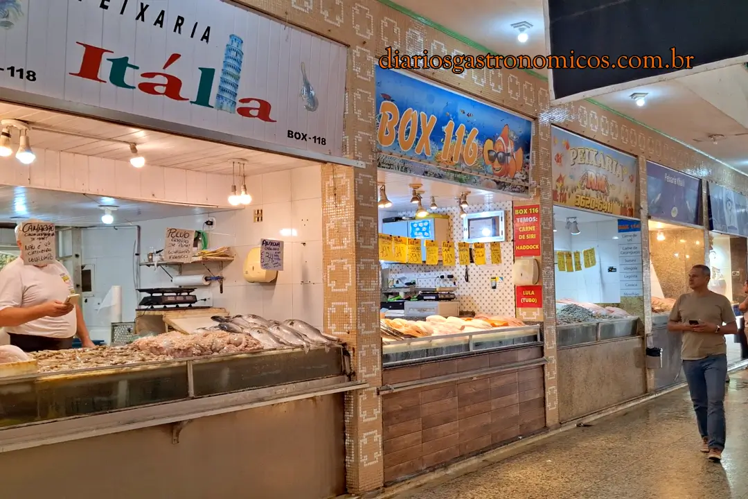 Peixarias do Mercado de Peixe de Niterói, Fish market stall with fresh seafood on ice, a vendor behind the counter, and signs in Portuguese.