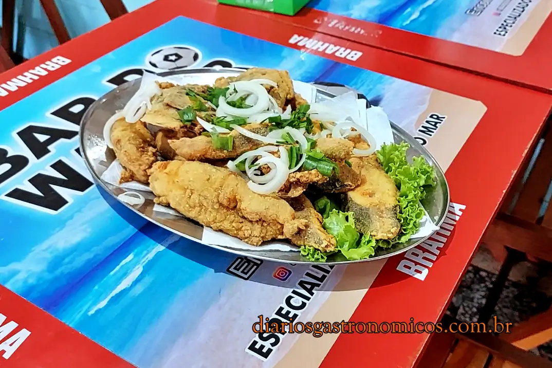 Porção de peixe frito, no Bar do Wagner, Mercado de Peixe de Niterói, Rio de Janeiro, Plate of fried fish pieces topped with onion rings and chopped herbs, served on a bed of lettuce on a metal tray.