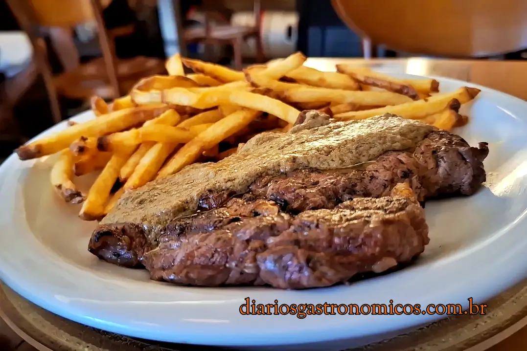 L'Entrecote com fritas do Demi Boteco, boteco de comida francesa no Largo do Machado, no Rio de Janeiro. Plate with two grilled steaks and a mound of golden french fries; restaurant setting, watermark diariosgastronomicos.com.br