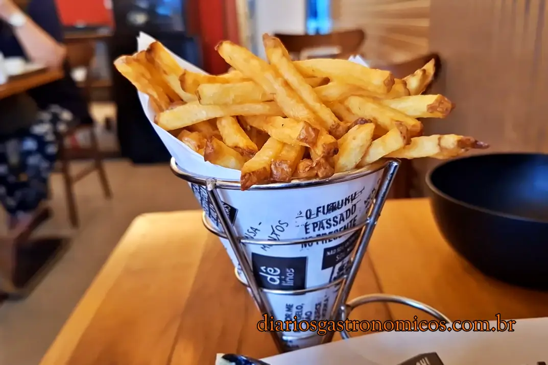 porção de batatas fritas do Demi Boteco, boteco de comida francesa no Catete, no Rio de Janeiro. Pile of golden French fries in a metal cone lined with newspaper wrap on a wooden table at a restaurant.