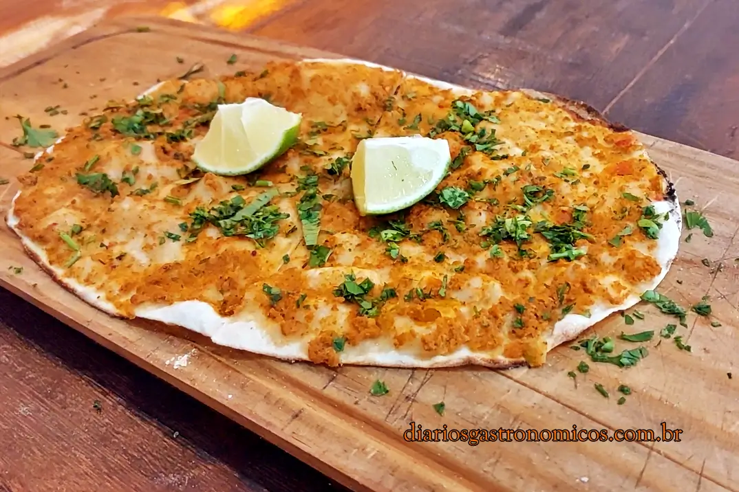 Lahmacum, tipica comida turca, chamada de esfiha de Antáquia, Crispy flatbread with garlic crumb topping and chopped parsley on a wooden board, garnished with lime wedges on top.