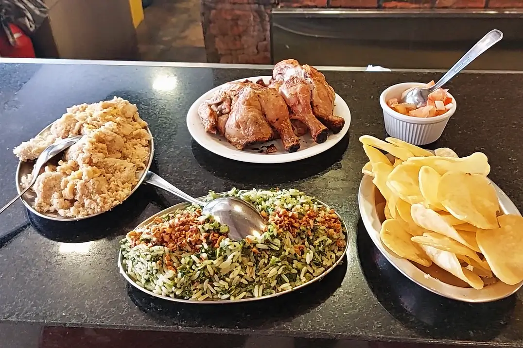Mesa com galeto, arroz de brócolis, farofa, batata portuguesa e molho à campanha no Quick Galetos, restaurante tradicional de Copacabana.