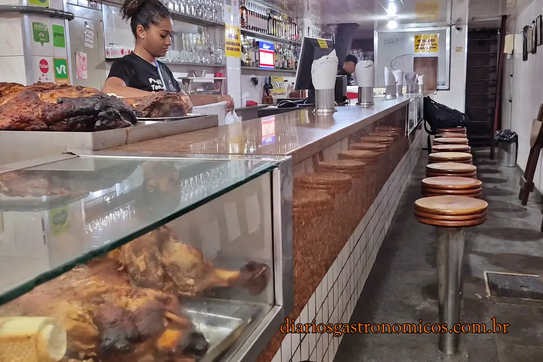 Interior do Opus, tradicional bar do Centro do Rio de Janeiro, com balcão de granito, bancos altos e peças de pernil expostas.