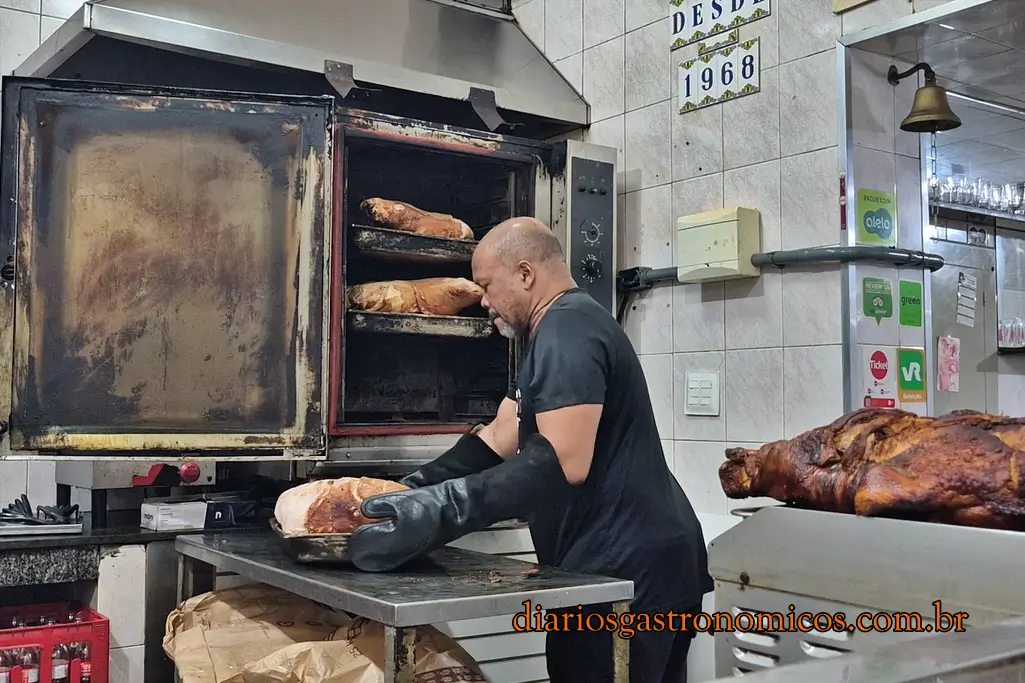 Funcionário do Opus retirando peças de pernil do forno onde são assadas lentamente durante várias horas.