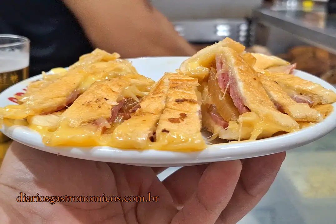 Sanduíche Pinheirinho servido no Opus, preparado com salame, queijo, cebolas, molho especial e abacaxi. Legenda