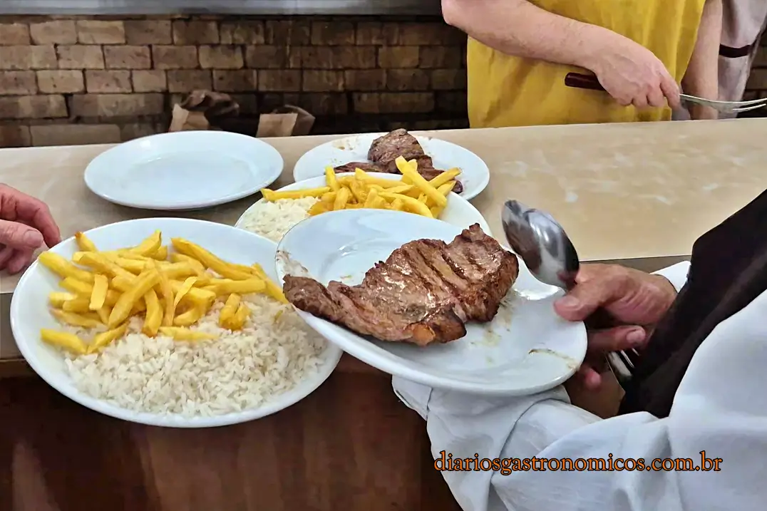 Garçom servindo prato de alcatra com arroz e batatas fritas no restaurante Churrasqueto em São Paulo.
